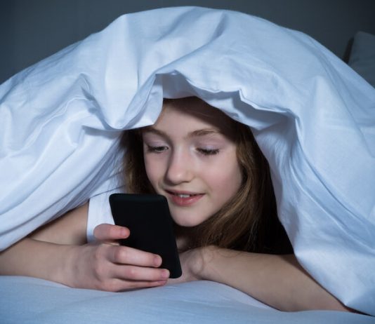 Une collègienne consultant son smartphone en cachette durant la nuit.